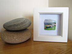 two rocks sitting on top of a wooden table next to a white frame with an image of a farm