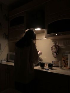 a woman standing in a kitchen at night with her hand on the counter and lights on