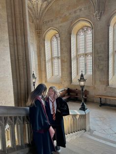 two women are standing on the stairs in an old building with stained glass windows and stone columns