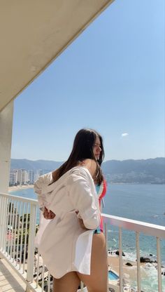 a woman standing on a balcony next to the ocean with her back turned and looking at something