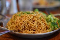 a bowl filled with noodles and broccoli on top of a wooden table