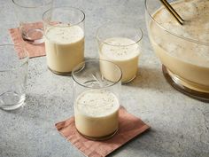 four glasses filled with liquid sitting on top of a counter next to a bowl and spoon