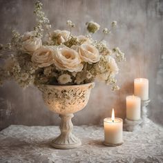 a vase filled with lots of white flowers next to two candles on top of a table