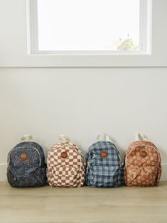 four backpacks lined up in a row on the floor next to a white wall