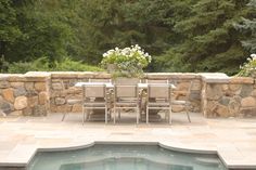 an outdoor dining table and chairs next to a swimming pool with stone walls around it