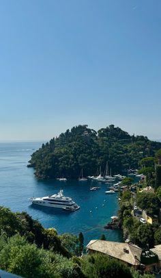 boats are docked in the blue water next to some houses and trees on a hill