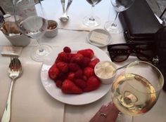 a white plate topped with strawberries next to two glasses of wine and silverware