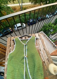 a green crocheted sweater sitting on top of a wooden table next to a window