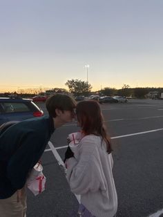 two people standing in a parking lot kissing each other