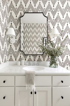 a bathroom with white cabinets and black and white wallpaper on the walls, along with a large mirror over the sink