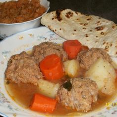 a plate with meat, potatoes and carrots next to a pita bread