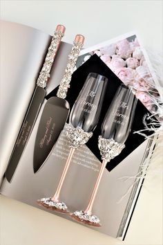 an open book with two wine glasses and a spoon on it next to a bouquet of flowers