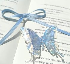 an open book with a butterfly brooch on it's cover and blue ribbon