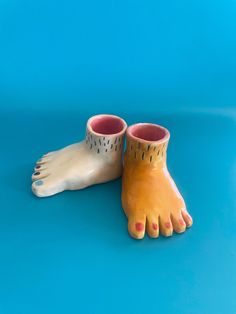 two ceramic feet are sitting on a blue surface, one is yellow and the other is pink