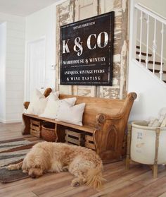 a dog laying on the floor in front of a wooden bench with pillows and a sign above it