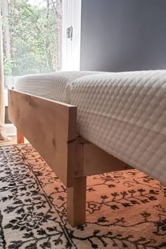 a wooden bed frame sitting on top of a carpeted floor next to a window