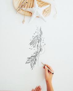 a person is drawing something on a piece of paper next to shells and seashells