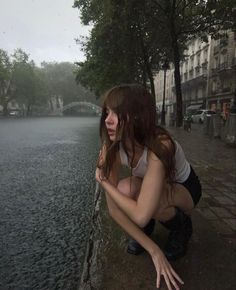 a woman squatting down next to a body of water with her hand on the ground