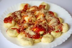 a white plate topped with ravioli covered in marinara sauce and parmesan cheese