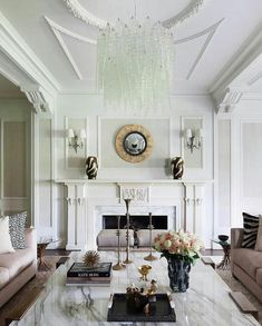 a living room filled with furniture and a chandelier hanging from the ceiling in front of a fire place