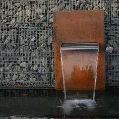 a water fountain is shown in front of a wall made of rocks and metal mesh