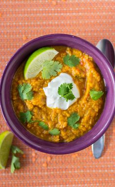 a purple bowl filled with food and garnished with cilantro, sour cream and lime