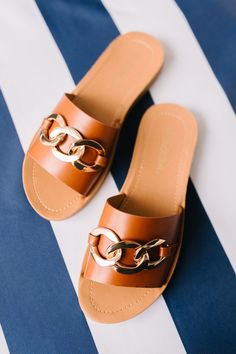 a pair of brown sandals on top of a blue and white striped blanket with gold chains