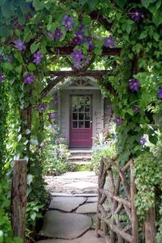 the entrance to a house is surrounded by greenery and stone walkways with purple flowers on either side