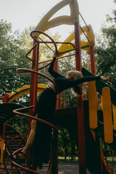 a woman climbing up the side of a wooden playground structure on top of a yellow and red slide