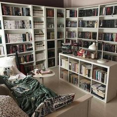 a living room filled with lots of books on top of white shelves next to a couch