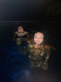 two people floating in the water at night with their heads turned to look like they are smiling