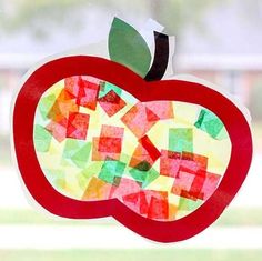 an apple made out of colored paper on a window sill in front of a grass field