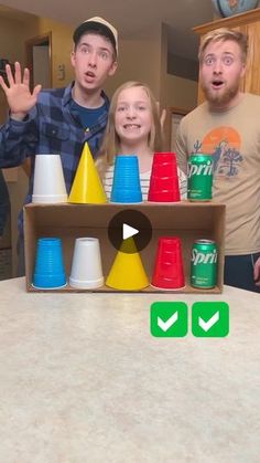 three people standing in front of a table with cups on it and one person holding their hands up