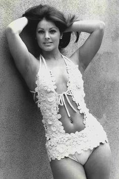 a woman in a white bathing suit leaning against a wall with her hands on her head