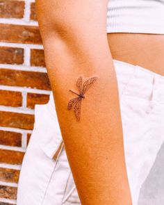 a woman's arm with a small dragonfly tattoo on the left side of her arm