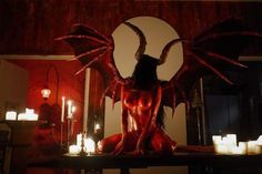 a demonic demon sitting on top of a table surrounded by candles