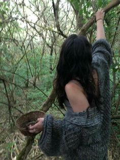 a woman in the woods reaching up to grab something out of a bowl that she is holding