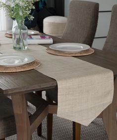 a dining room table with plates and flowers in a vase on the top, along with other place settings