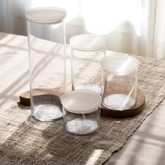 three clear glass containers sitting on top of a wooden tray next to a window with white curtains