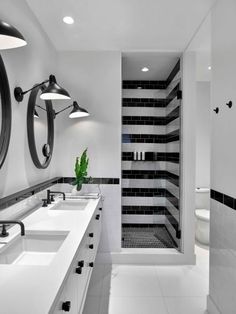 a bathroom with black and white tiles on the walls, two sinks and a large mirror