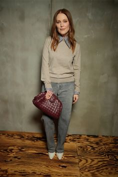 a woman holding a red purse standing on top of a wooden floor next to a wall