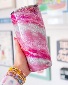 a woman holding up a pink and white cup with glitter on the inside, in front of a wall full of pictures