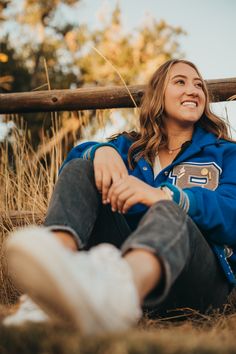 a woman sitting on the ground in front of a wooden fence and smiling at the camera