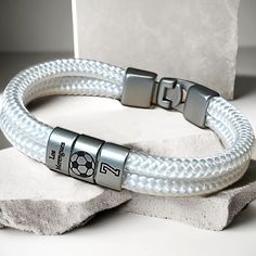 a white braided leather bracelet with two metal clasps on top of a rock