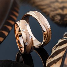 two gold wedding bands with diamonds on them sitting on a black surface next to a zebra print pillow