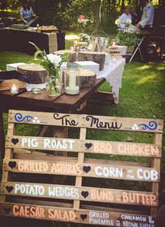 a wooden table topped with lots of different types of food and drinks on top of grass