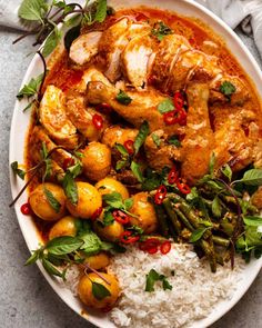 a white plate topped with chicken and potatoes covered in sauce, garnished with green leaves