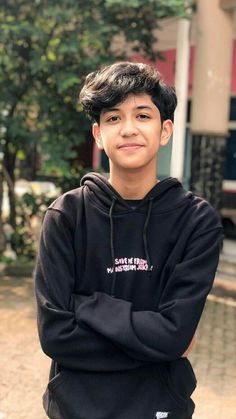 a young boy standing in front of a building with his arms crossed and looking at the camera