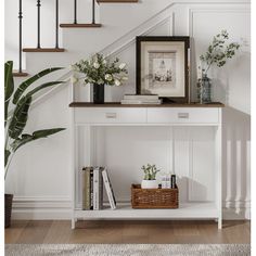 a white shelf with books and flowers on it in front of some stairs, next to a potted plant