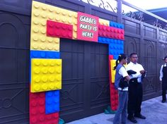 some people are standing in front of a building made out of legos and bricks